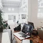 A bright, modern workspace featuring laptops, a camera, and a drawing tablet in an indoor office.